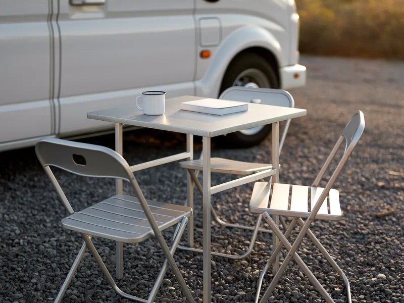 Tavolo pieghevole in alluminio con due sedie accanto a un camper